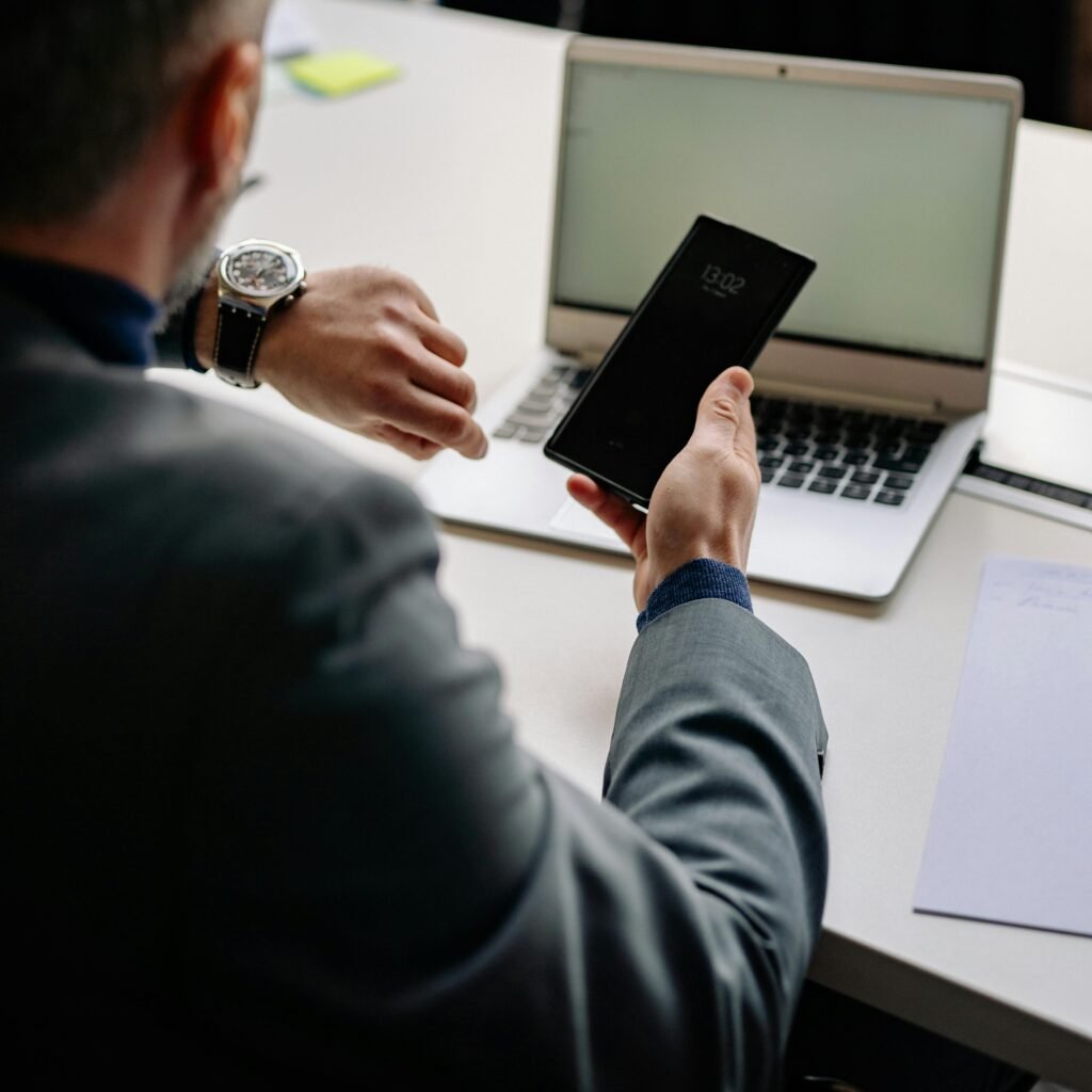 pexels-photo-7794018-7794018 Man in office using smartphone and laptop, showing time management.